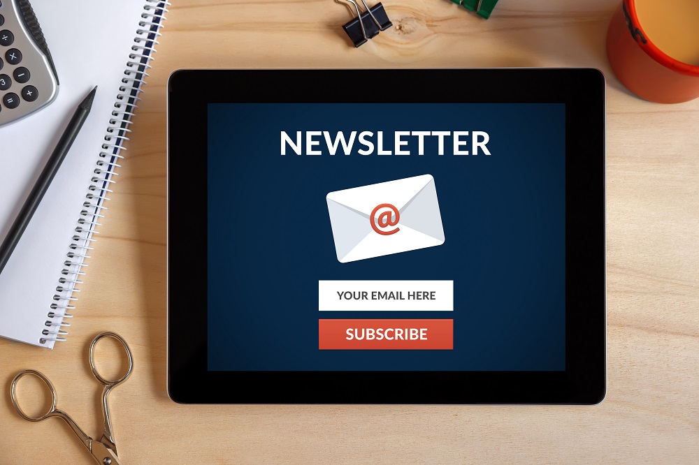 Subscribe to newsletter on tablet screen with office objects on wooden desk.