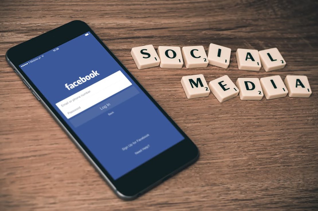 Facebook login screen on mobile device with social media in tiled letters on wooden desk